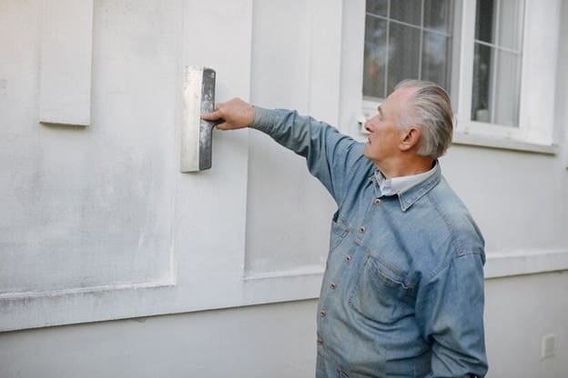 A man in blue shirt painting the side of a house.