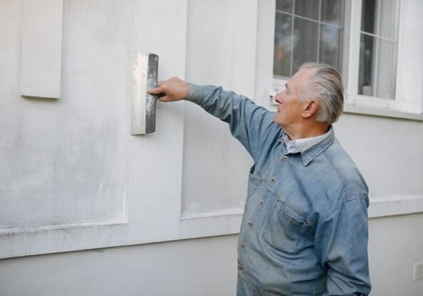 A man in blue shirt painting the side of a house.