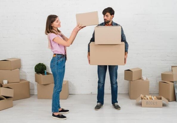 A woman playfully handing a box to a man holding multiple boxes.